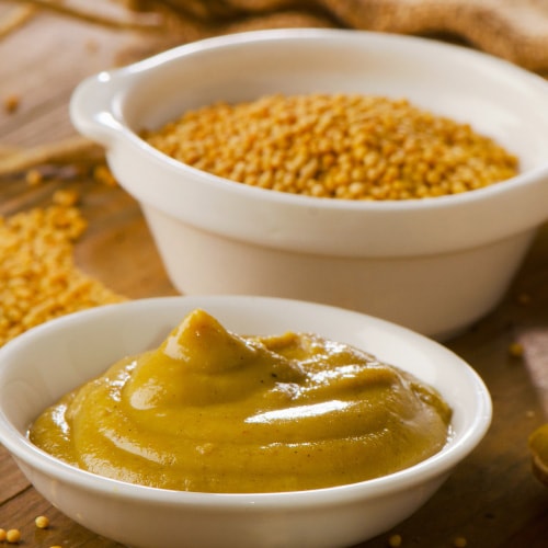 bowl of mustard seeds next to a bowl of prepared mustard