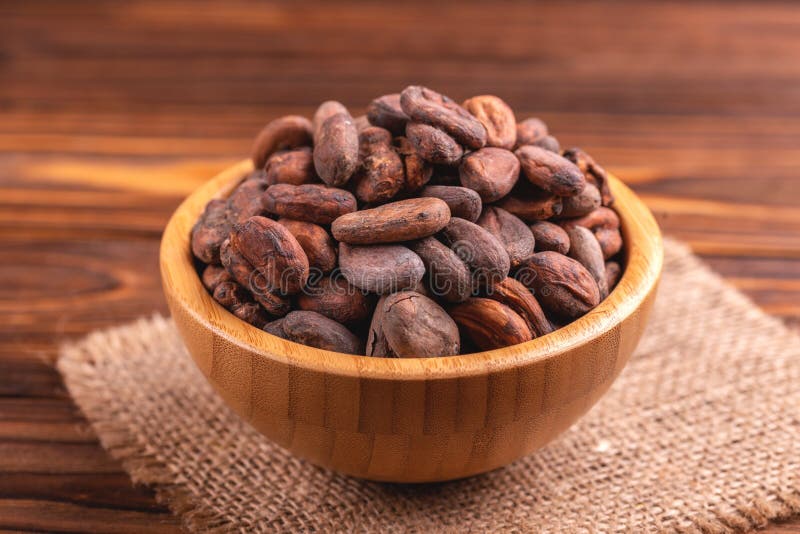 Bowl full of aromatic raw cocoa beans with burlap napkin. On wooden background. Horizontal view. Copy space stock photo
